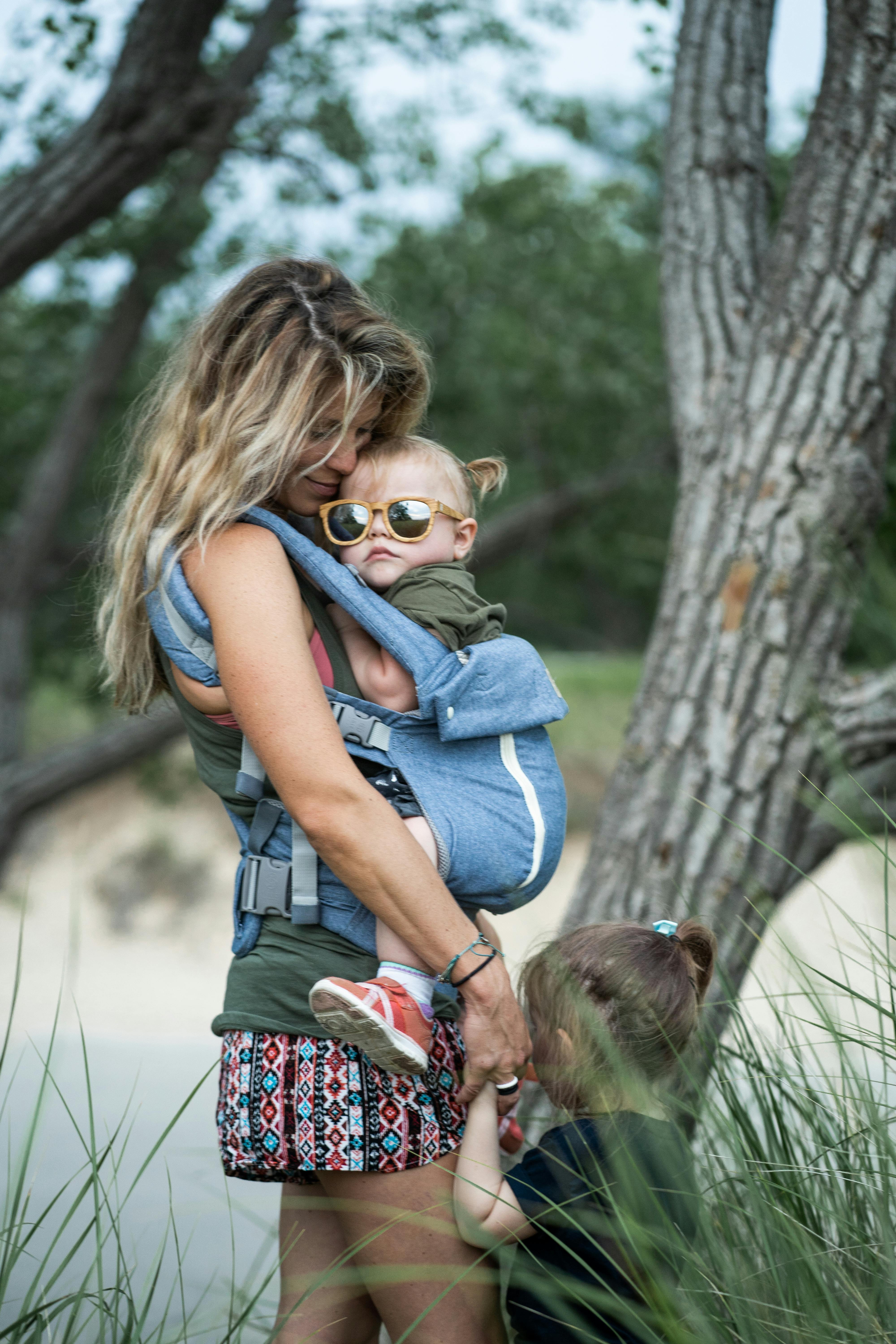 Top Picks for Tots 🛒✨: Mom carrying baby in a carrier on a beach, surrounded by nature.